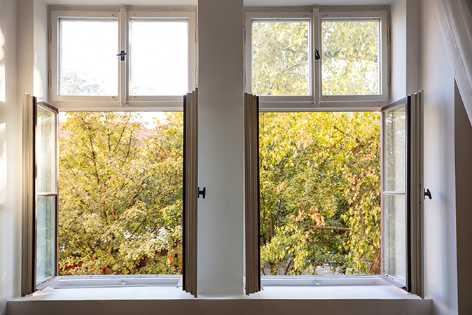 An open window in a home for sale showcases large trees in the yard.