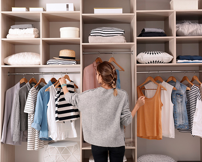 A woman rummages through clothes in a cluttered wardrobe closet.