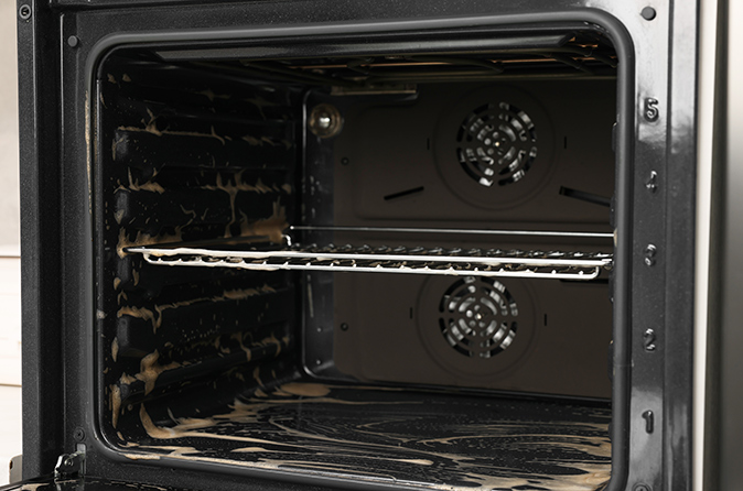 An open electric oven covered with cleaning foam in a kitchen.