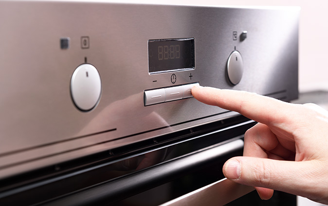 A male finger pressing a button on control panel on an oven.