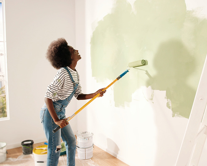 A homeowner uses a roller to paint a wall in her home.