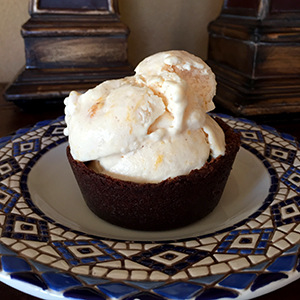 Fresh peach ice cream in a brownie bowl displayed on stylish blue plate.
