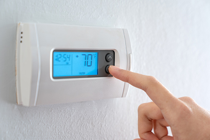 A close-up of a person’s finger pressing a button to lower the temperature on a thermostat.