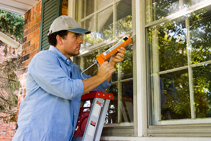 A man caulking the windows at his house for sealing