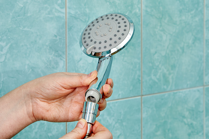 A close up of a person’s hands connecting a new flat showerhead to a flexible hose.
