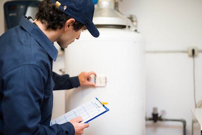 A plumber checking the temperature setting on a water heater.