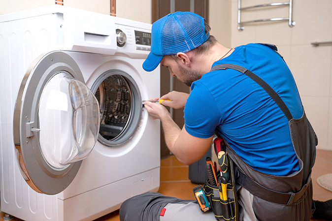 Plumber using a screwdriver to fix a washing machine.