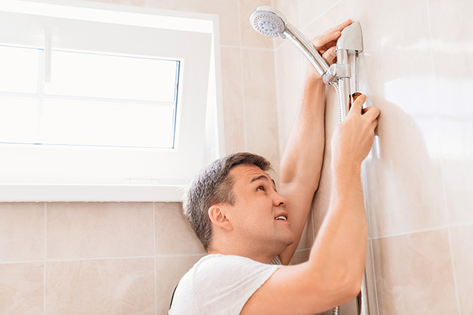 A plumber using a screwdriver to install a showerhead in a bathroom.