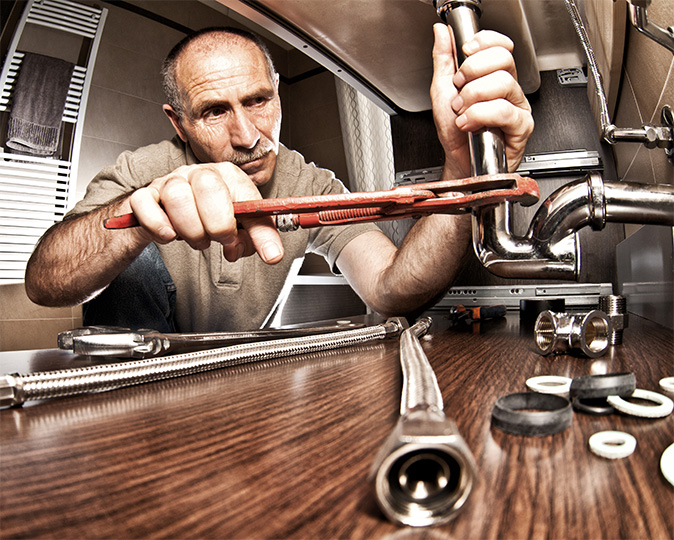 A repair technician reassembles the pipework underneath a kitchen sink.