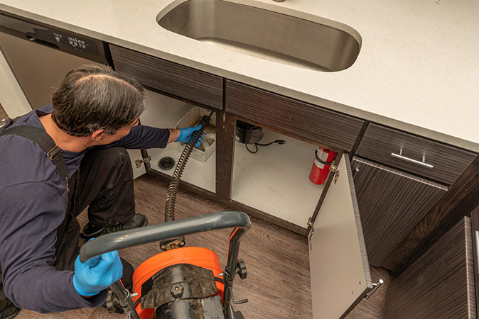 A man fixing the main drain line with a sewer auger.