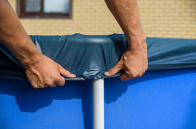 A man stretches a sturdy pool cover over an above-ground pool.
