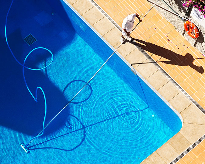 A professional using a pool vacuum on an extended pole is cleaning a home swimming pool.