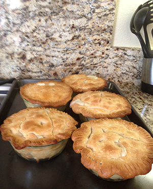 Image of 5 fresh-baked potpies on a baking sheet set on a granite kitchen counter.