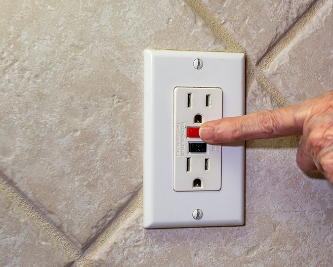 A closeup of the reset button on a GFCI outlet being pressed by a homeowner.