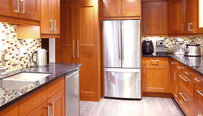 A brightly lit stainless steel refrigerator in modern kitchen against a backdrop of warm brown cabinets.