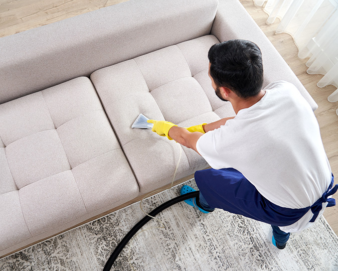A professional cleaner steam cleans a living room couch in a brightly lit room. 