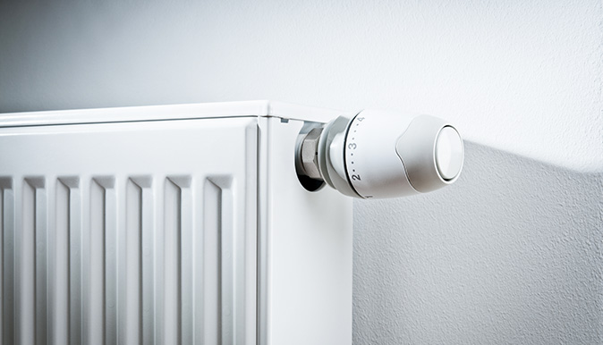 A modern white radiator with a thermostat set against a white wall.
