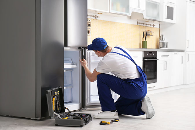 Refrigerator technician works to repair door on a rental property’s fridge.