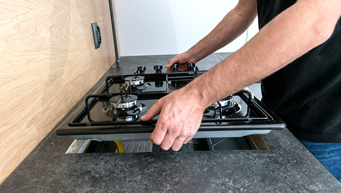 A homeowner lifts his stovetop to find the gas shut-off valve underneath.