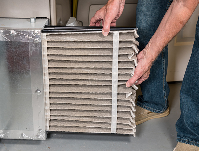 A person removing a dirty air filter from a furnace.