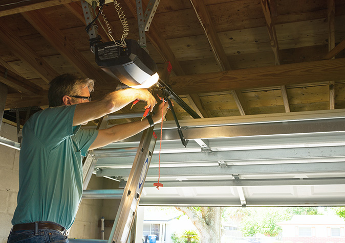 A repairman on a ladder working on a garage door opener.
