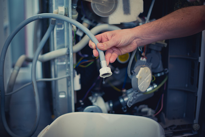 A maintenance person is repairing a leaky dishwasher.