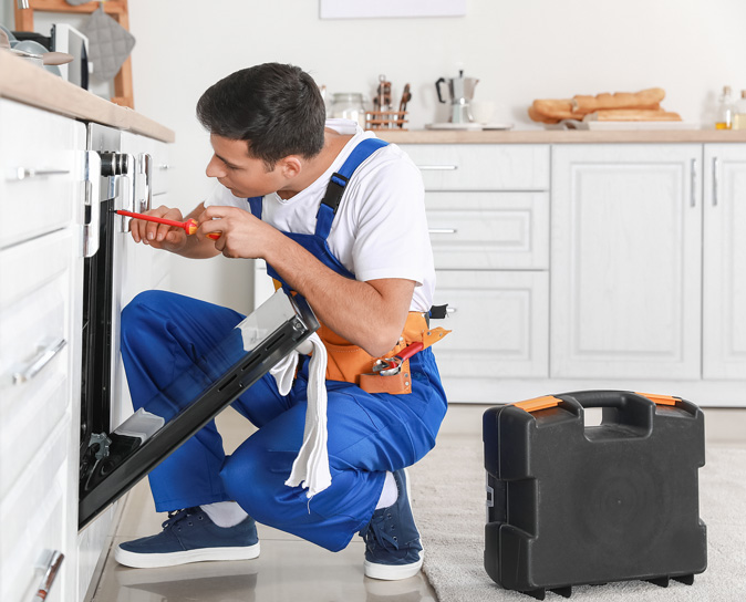 A repairman works on an electric oven in a kitchen. 