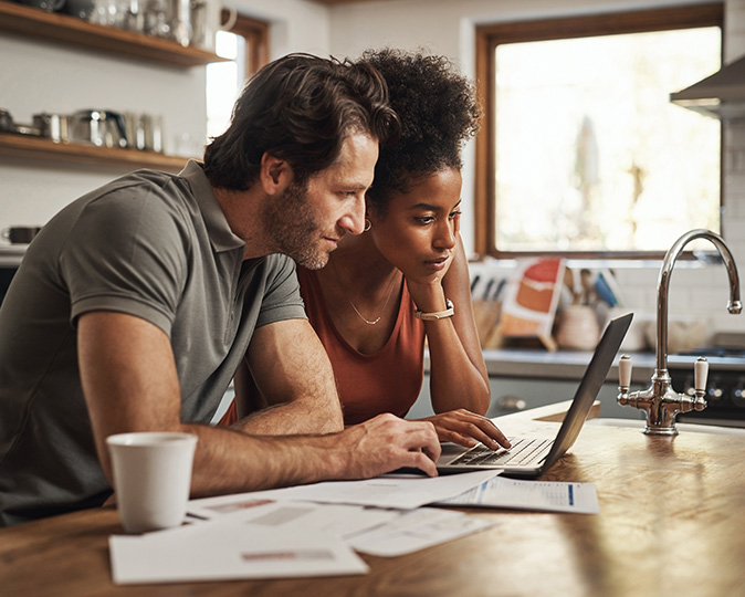 A couple at the kitchen counter looks over financial documents for buying a home. 