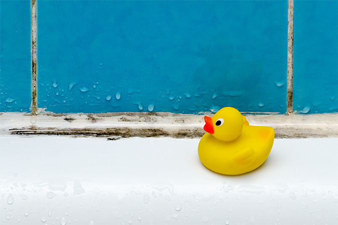 Tile around a bathtub shows grout and caulking spotted with black and brown mold.