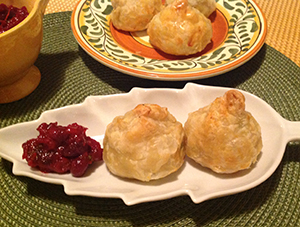 Image of freshly made samosas on a white plate shaped as a decorative leaf, with a side of cranberry chutney sauce.