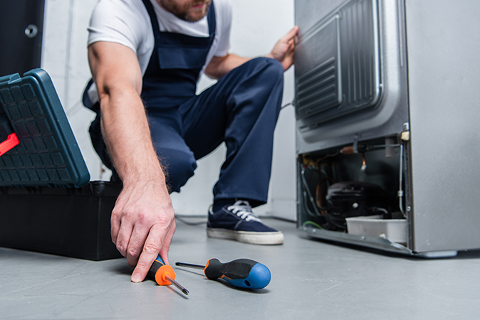 A technician inspecting a refrigerator unit reaches for a screwdriver.