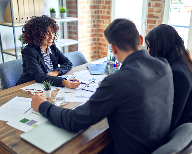 A couple sits at a desk with a lender, going over paperwork.