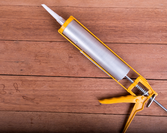 A silver and yellow caulk gun on a wood background.