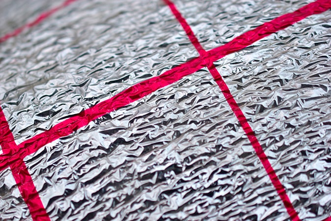 A close-up of silver thermal insulation material with red stripes that serves as a thermal barrier in basement walls.