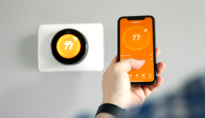 Person adjusting their smart thermostat using their cell phone.