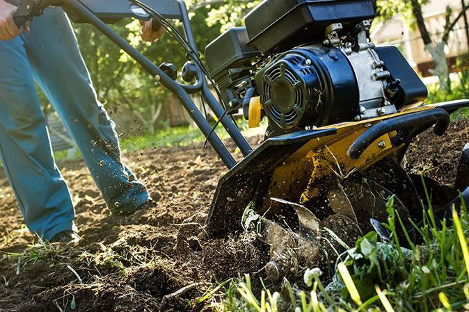 A homeowner tills their garden with a motored cultivator.