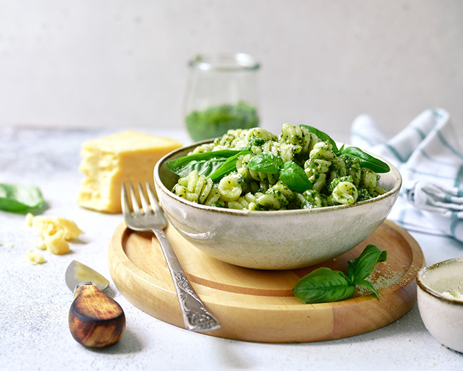 Vibrant green pesto pasta garnished with fresh basil leaves.