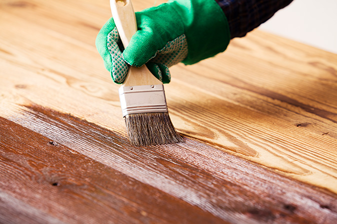 A person holding a brush painting on a newly sanded wood floor to match the tone with the rest of the wood