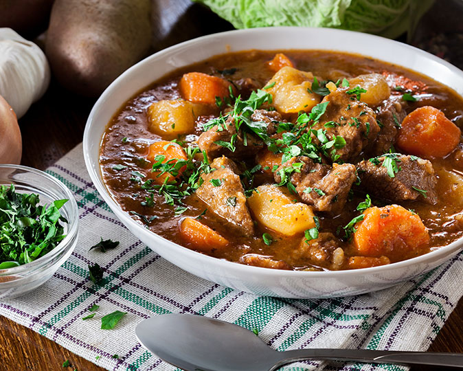 A white bowl is full of a delicious Irish stew with a green garnish.