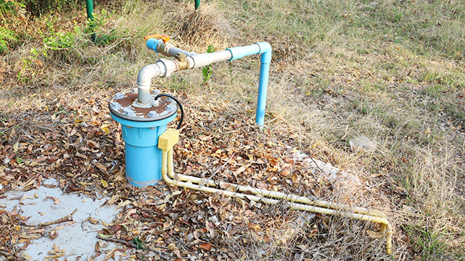 A submersible well pump on a concrete slab covered by leaves in a yard.