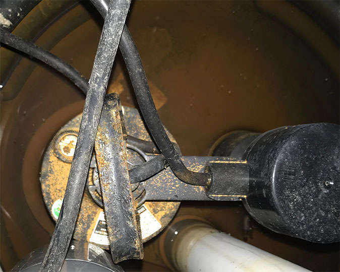 A flashlight illuminates a residential sump pump in a basement.