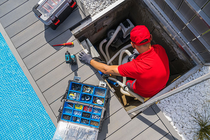A professional pool inspector surrounded by tools looking at the pool equipment.