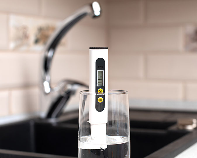 A TDS meter that measures water hardness floats atop a glass of tap water in a kitchen.
