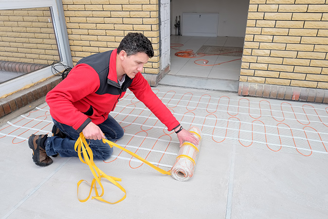 A man is kneeling on floor while he installs an electric heating cable.