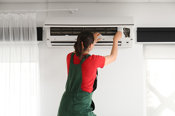 A service technician repairing an indoor air conditioner unit for a homeowner.