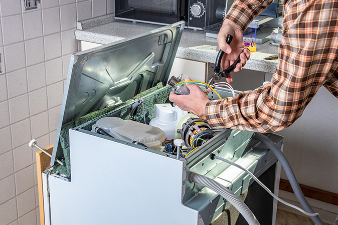 A technician repairs a broken dishwasher.