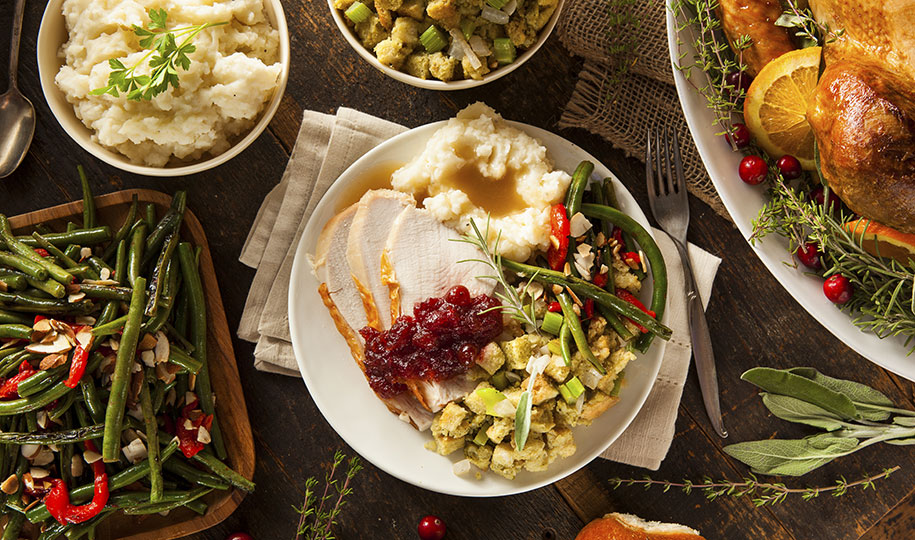 Image shows a white plate brimming with Thanksgiving leftovers with side dishes surrounding main plate.