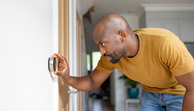 A homeowner bends down to check his digital smart thermostat.