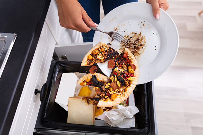 A woman putting food waste into a trash can.