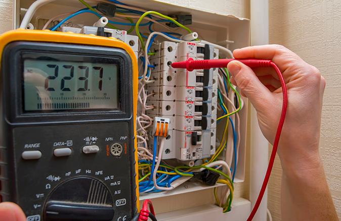 A closeup shows a hand holding a tool for measuring home voltage.